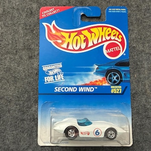May include: A Hot Wheels Second Wind die-cast car on a blue and red card. The white car has a blue interior and the number 6 on the side. The card reads "Coolest to Collect!" and "Guaranteed for Life."