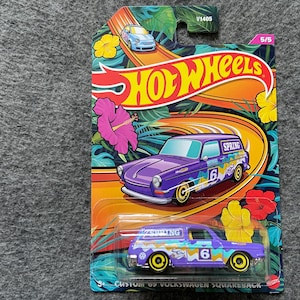May include: A purple and yellow Hot Wheels die-cast toy car with "Custom '62 Volkswagen Squareback" and "Spring" printed on the side. The car is on a white background with a green, yellow, and blue floral design.
