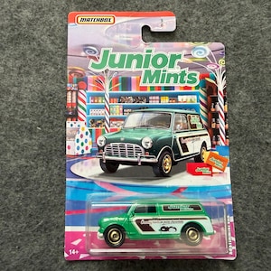May include: Matchbox toy car set featuring a green and white Mini Cooper and a green and white van, both branded "Junior Mints." The packaging includes the "Junior Mints" logo and a candy shop background.