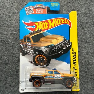 May include: A Hot Wheels Off-Road truck toy in a package. The die-cast vehicle is tan with black accents, large off-road tires, and the number 66. The packaging is blue and yellow with the Hot Wheels logo and the text "OFF-ROAD".