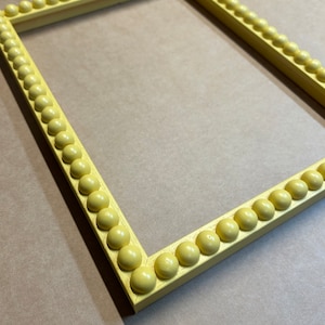 Pode incluir: Uma moldura de imagem amarela com uma borda de contas. A moldura &eacute; feita de madeira e tem um design simples e elegante.