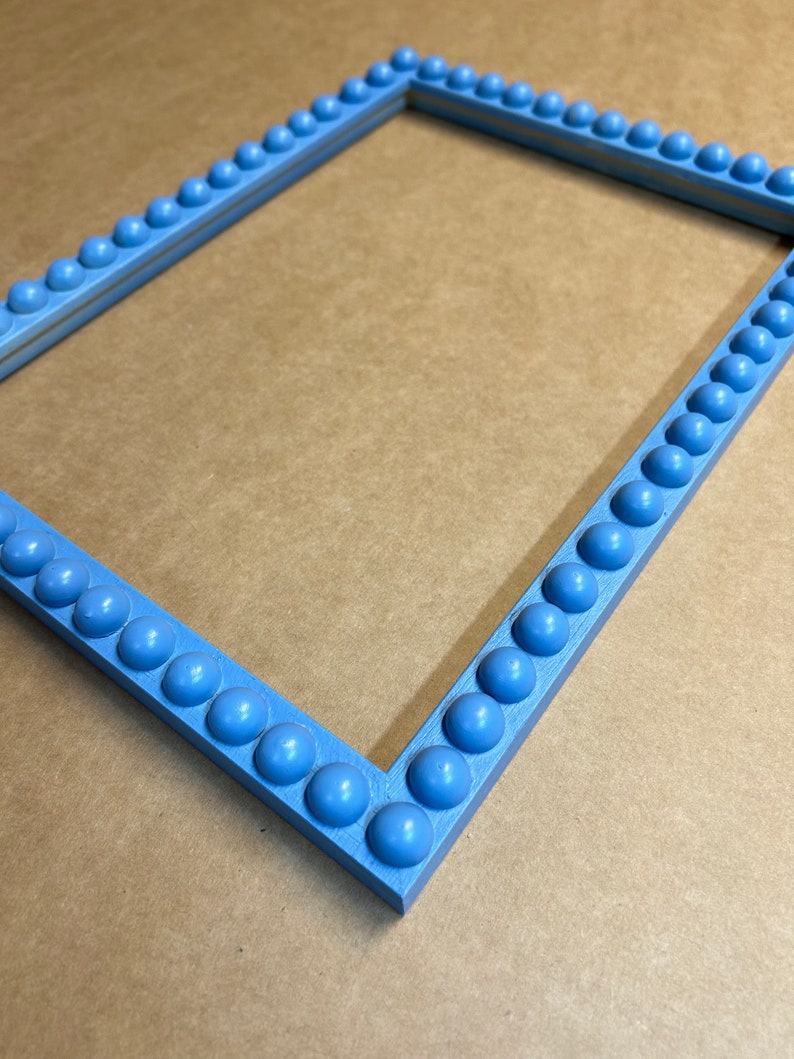 Pode incluir: Uma moldura de imagem azul claro com uma borda de contas decorativas. A moldura &eacute; feita de madeira e tem um design simples e elegante.