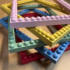 Pode incluir: Quatro molduras de fotos empilhadas umas sobre as outras. As molduras s&atilde;o de madeira e t&ecirc;m uma borda de contas. As molduras s&atilde;o pintadas em cores diferentes: rosa, amarelo, verde e azul.