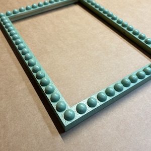 Pode incluir: Uma moldura de imagem verde claro com uma borda de contas decorativas. A moldura &eacute; feita de madeira e tem um acabamento desgastado.