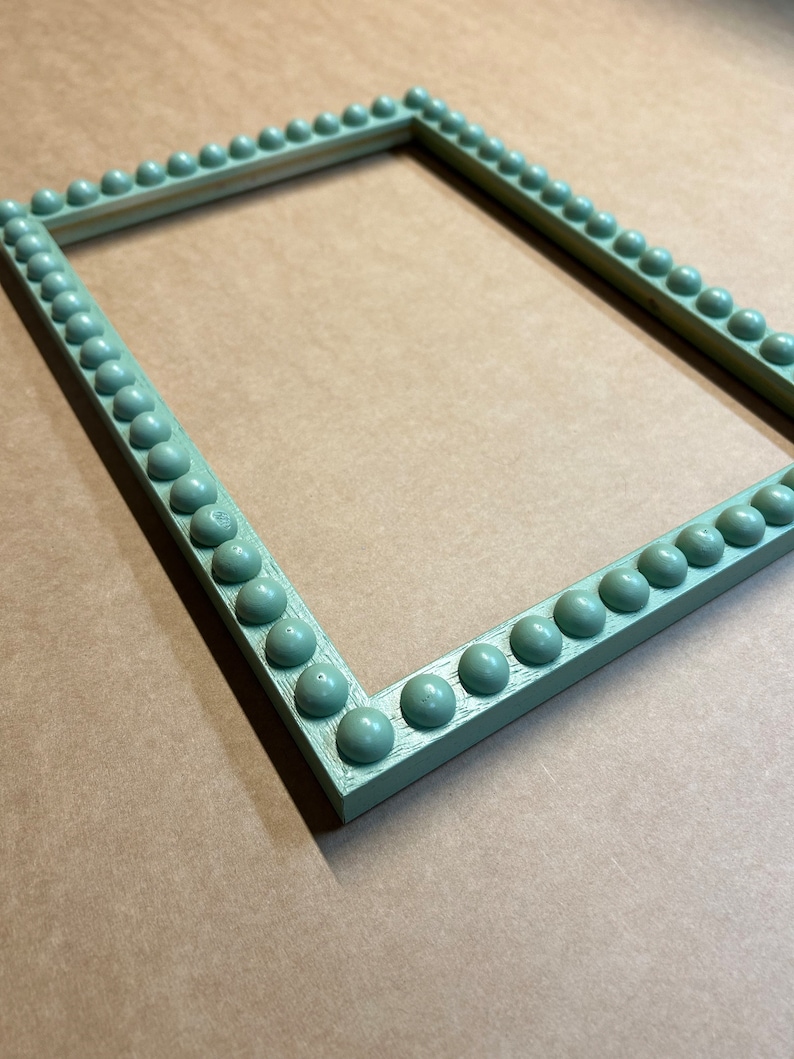 Pode incluir: Uma moldura de imagem verde claro com uma borda de contas decorativas. A moldura &eacute; feita de madeira e tem um acabamento desgastado.