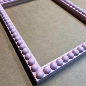 Pode incluir: Uma moldura de imagem rosa com uma borda de contas. A moldura &eacute; feita de madeira e tem um acabamento liso.