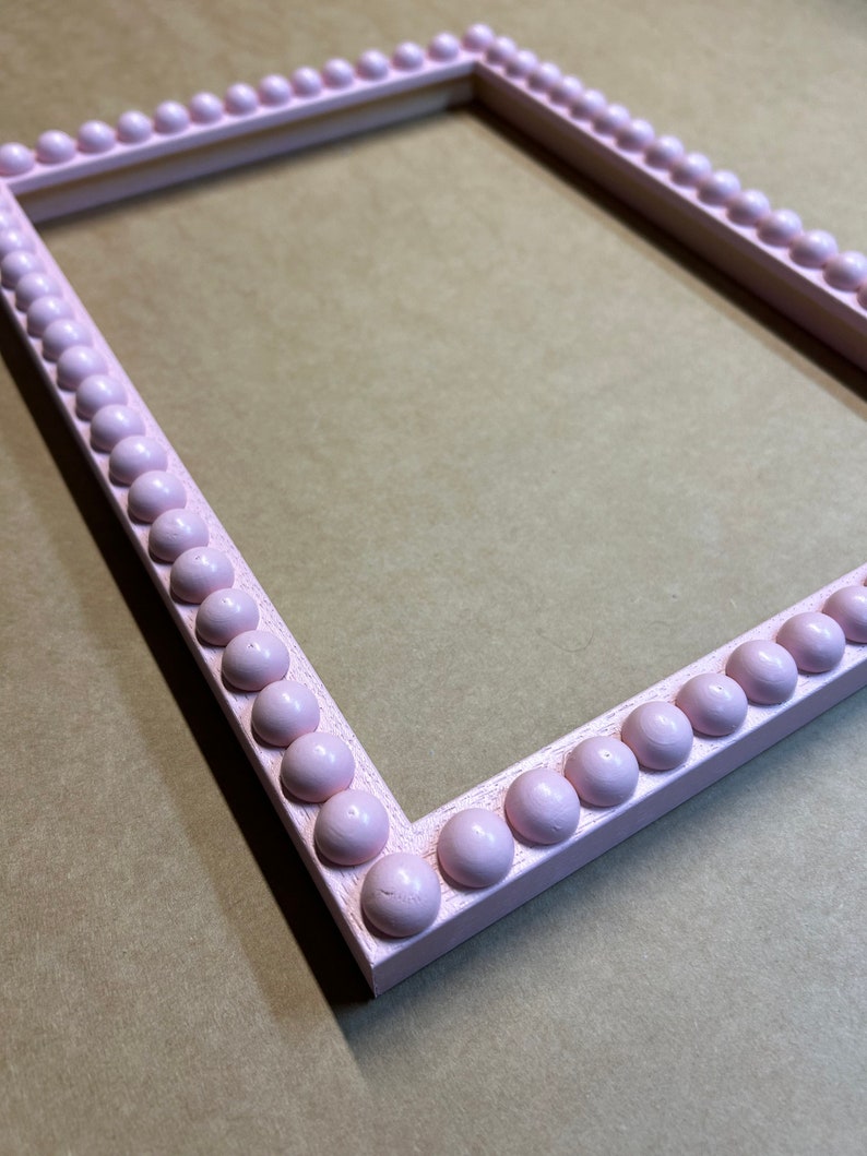 Pode incluir: Uma moldura de imagem rosa com uma borda de contas. A moldura &eacute; feita de madeira e tem um acabamento liso.