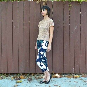 May include: A woman wearing a beige, patterned, short-sleeved shirt and black and white floral cropped pants. She is wearing sunglasses and black flats.