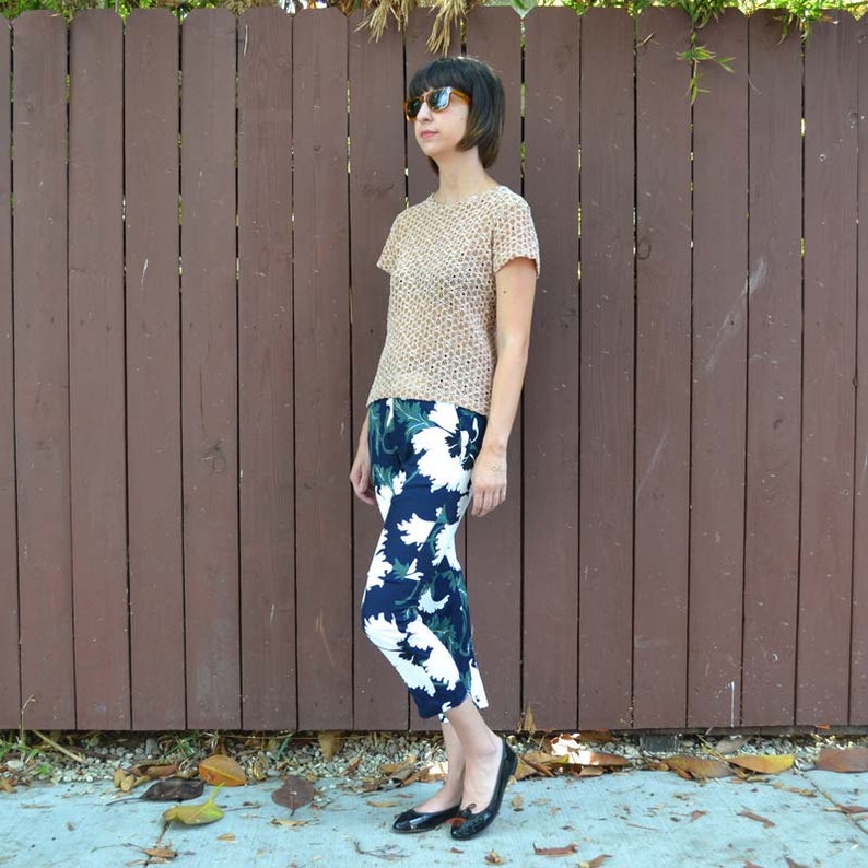 May include: A woman wearing a beige, patterned, short-sleeved shirt and black and white floral cropped pants. She is wearing sunglasses and black flats.