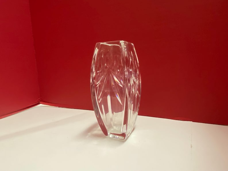 May include: A clear glass vase with a geometric pattern. The vase is rectangular in shape and has a square base.