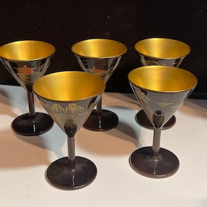 May include: Set of six black and gold Japanese sake cups with intricate designs. The cups are made of lacquered wood and have a gold rim.