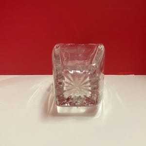 May include: A clear glass square vase with a cut glass design. The vase is empty and has a reflective surface.