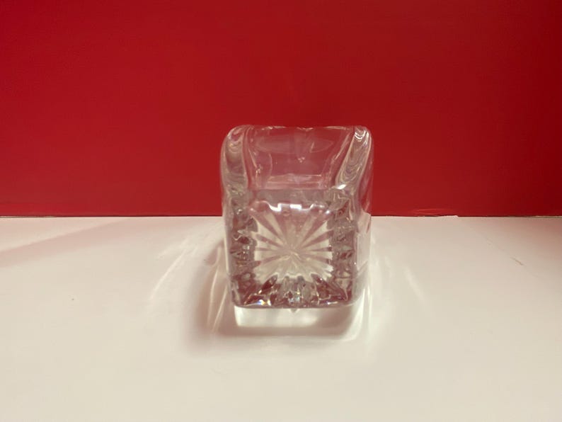 May include: A clear glass square vase with a cut glass design. The vase is empty and has a reflective surface.