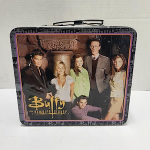 May include: A rectangular metal lunch box featuring a group photograph of the cast of Buffy the Vampire Slayer. The front panel displays the show title in yellow text and five characters standing in front of a stone pillar and dark background.