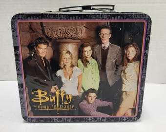 May include: A rectangular metal lunch box featuring a group photograph of the cast of Buffy the Vampire Slayer. The front panel displays the show title in yellow text and five characters standing in front of a stone pillar and dark background.