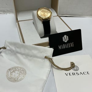 Pu&ograve; includere: Un orologio Versace color oro con cinturino in pelle nera, presentato in una scatola bianca con il logo Versace. Include un sacchetto bianco con coulisse con un emblema dorato della testa di Medusa, una carta nera Madaluxe e un libretto Versace.