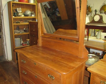 May include: A vintage wooden dresser with a mirror and three drawers. The dresser has a carved design on the top and brass handles on the drawers.