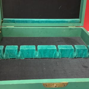 Może przedstawiać: Zielone drewniane pudełko z czarnym aksamitnym wnętrzem i rzędem zielonych aksamitnych przegródek. Pudełko jest otwarte, a przegródki są puste.