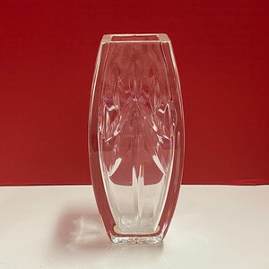 May include: A clear glass vase with a geometric design. The vase is tall and slender, with a rectangular base.