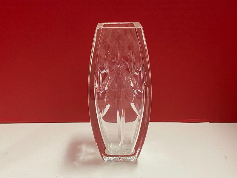 May include: A clear glass vase with a geometric design. The vase is tall and slender, with a rectangular base.