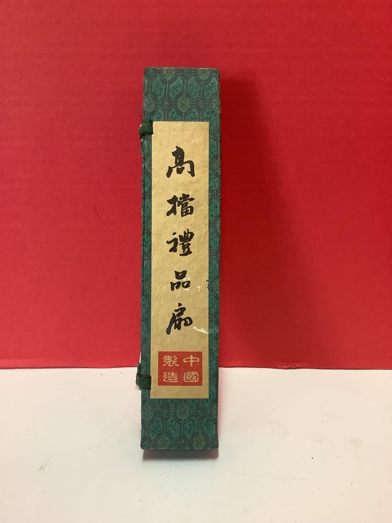 K&ouml;nnte beinhalten: Eine gr&uuml;ne Schachtel mit chinesischen Schriftzeichen auf einem wei&szlig;en Etikett. Der Text lautet "品 譜 珍 蔵" und "裝 中 國".