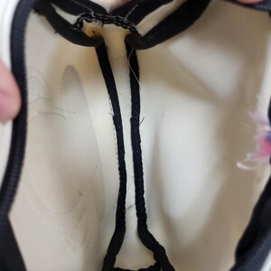 May include: Cream-colored bag interior with black trim and a zipper. The bag's interior is visible, showing the stitching and construction details. The black trim outlines the edges and zipper, creating a contrasting border.