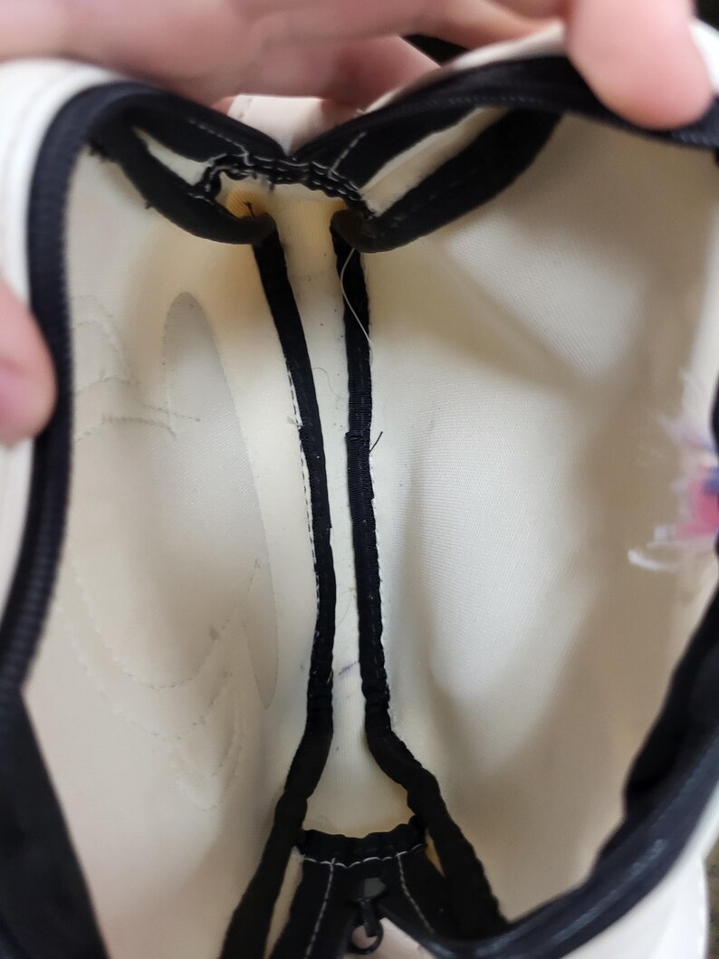 May include: Cream-colored bag interior with black trim and a zipper. The bag's interior is visible, showing the stitching and construction details. The black trim outlines the edges and zipper, creating a contrasting border.