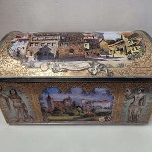 May include: A vintage, gold-coloured metal tin box with a domed lid. The lid features a colourful illustration of a medieval German town with the text "Die Dörfer am Würzberg". The sides of the box have illustrations of people in medieval clothing and a castle.