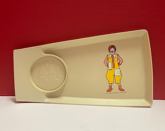 Może przedstawiać: Biała plastikowa taca z logo McDonald's i obrazkiem Ronalda McDonalda. Taca ma małe okrągłe wgłębienie na kubek.