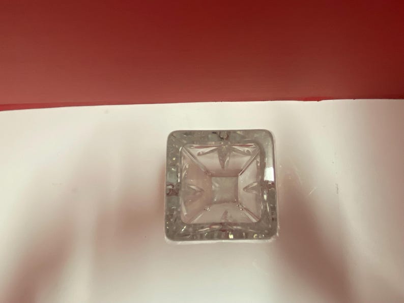 May include: A clear glass vase with a square base and intricate cut glass design.