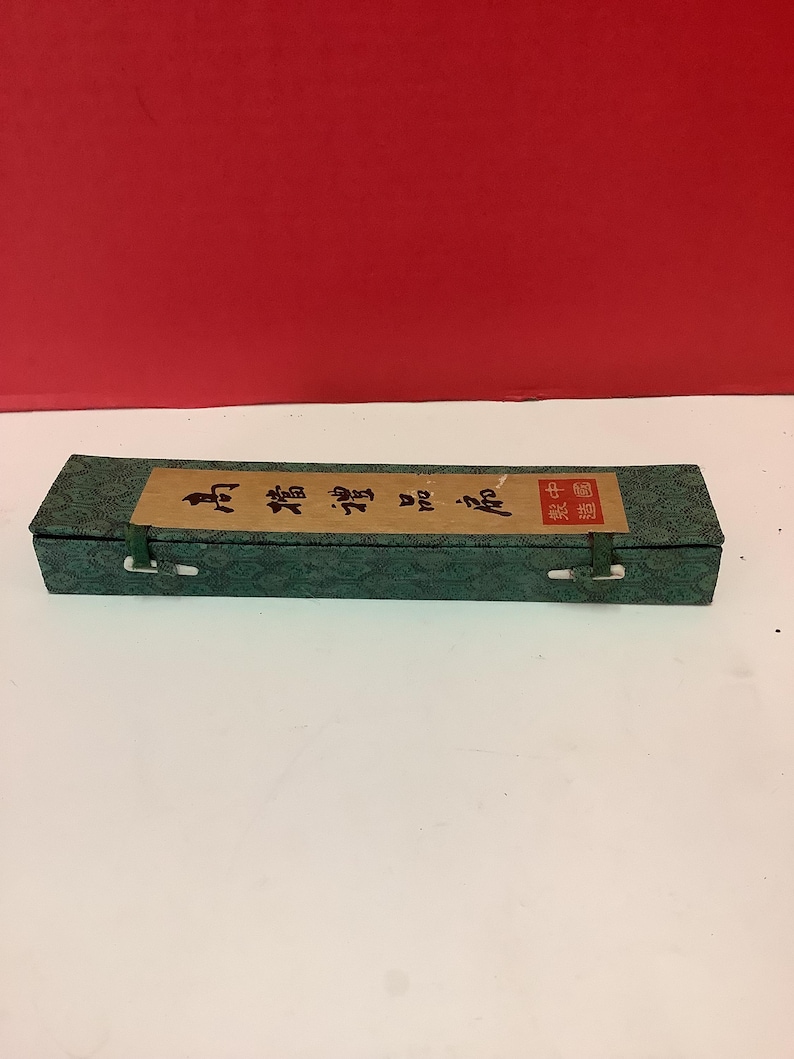 K&ouml;nnte beinhalten: Eine gr&uuml;ne Box mit einem braunen Etikett, auf dem in chinesischen Schriftzeichen "Chinesischer Kalligraphie-Pinsel" steht. Die Box hat zwei wei&szlig;e Verschl&uuml;sse an beiden Seiten.