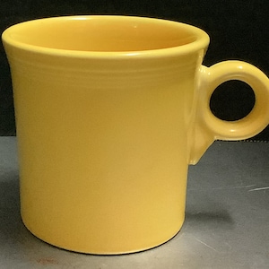 May include: A yellow ceramic mug with a rounded handle. The mug is a classic style with a simple design.