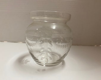 Puede incluir: Tarro de cristal transparente con diseño floral y de hojas grabado. El tarro tiene un cuerpo redondeado y un borde ligeramente ensanchado. El diseño grabado incluye un motivo floral central con hojas y líneas horizontales.