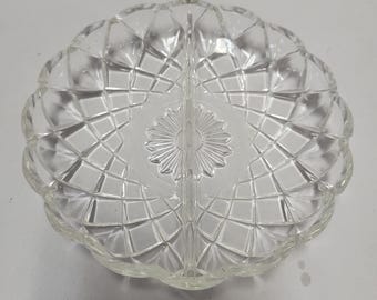 May include: Clear glass divided serving dish. The dish is round with a scalloped edge and a diamond pattern. The center has a starburst design, and the dish is divided into two sections.