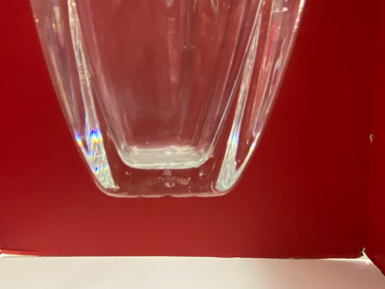May include: Clear glass vase with a geometric shape and a slightly iridescent finish. The vase has a square base and a rectangular body.