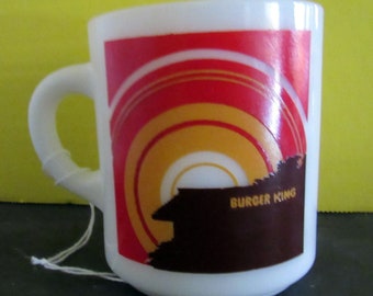 May include: White ceramic mug with a red, orange, and brown graphic design featuring a stylized sunset and the text "Burger King".