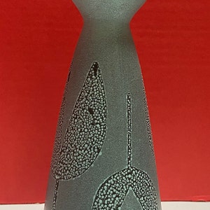 May include: A light blue ceramic vase with a wide mouth and a narrow base. The vase has a speckled glaze and a design of three stylized leaves in a darker shade of blue.