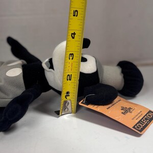 May include: A black, white, and gray plush toy, approximately 4 inches tall, of a cartoon character. The toy has a tag attached. The character is lying on its side.