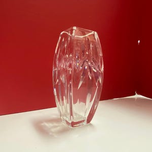 May include: A clear glass vase with a geometric design. The vase is empty and has a square base.