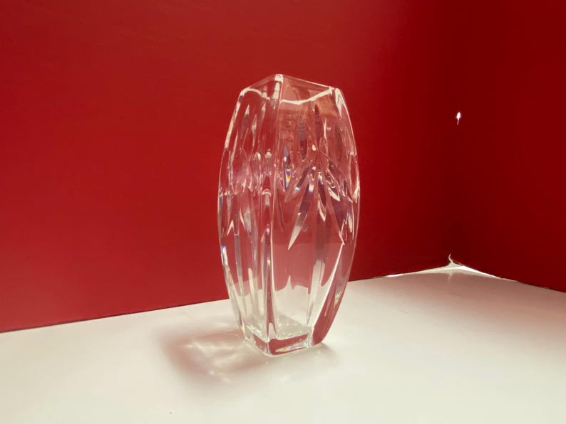 May include: A clear glass vase with a geometric design. The vase is empty and has a square base.
