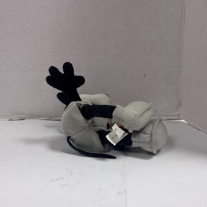 May include: A plush toy of a cartoon character, primarily black and white with gray accents. The character has large black ears, a black tail, and gray gloves and shoes. The toy is lying on its side.