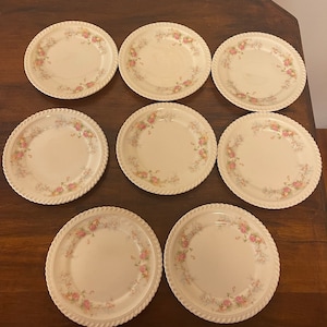 Könnte beinhalten: Set aus acht weißen Keramiktellern mit einem zarten Blumendesign in Rosa- und Grüntönen. Die Teller haben einen seilartigen Rand und sind perfekt für einen Vintage- oder Cottagecore-Look.