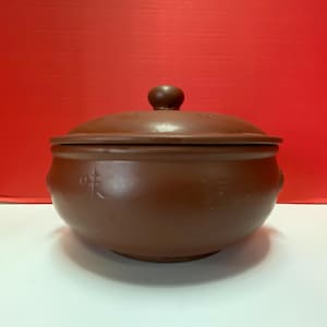 Könnte beinhalten: Ein brauner Keramiktopf mit Deckel. Der Topf hat chinesische Schriftzeichen an der Seite.