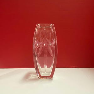 May include: A clear glass vase with a geometric pattern. The vase is tall and narrow, with a rectangular base.