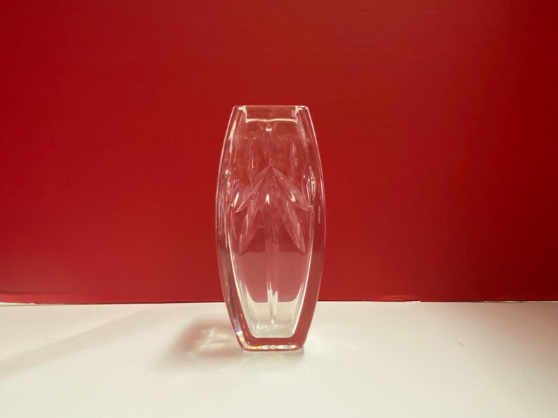 May include: A clear glass vase with a geometric pattern. The vase is tall and narrow, with a rectangular base.