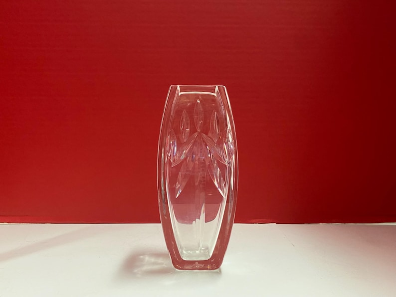 May include: A clear glass vase with a geometric pattern. The vase is tall and slender, with a rounded base and a flared top.
