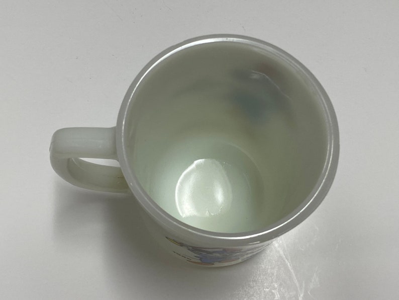 May include: White ceramic mug with a blue and yellow design. The mug has a handle and is empty.