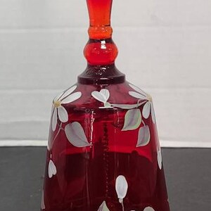 Puede incluir: Una campana de vidrio roja con un diseño floral blanco. La campana tiene una parte superior redondeada y una base ancha. El diseño floral presenta flores blancas y hojas sobre un fondo rojo.
