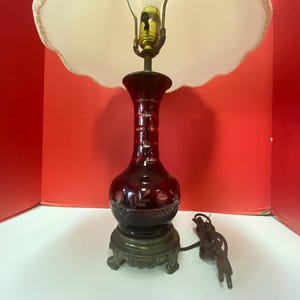 May include: A red glass table lamp with a white lampshade. The lamp has a decorative etched design and a brass base.