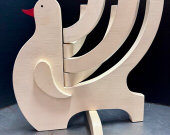 May include: White wooden dove menorah with a red beak and five candle holders. The dove is standing on a base with three legs.